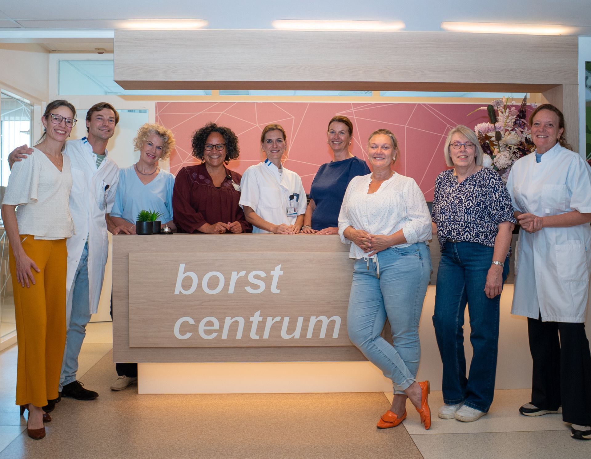 Groep mensen poseert voor het "Borstcentrum" bord in een medische omgeving.