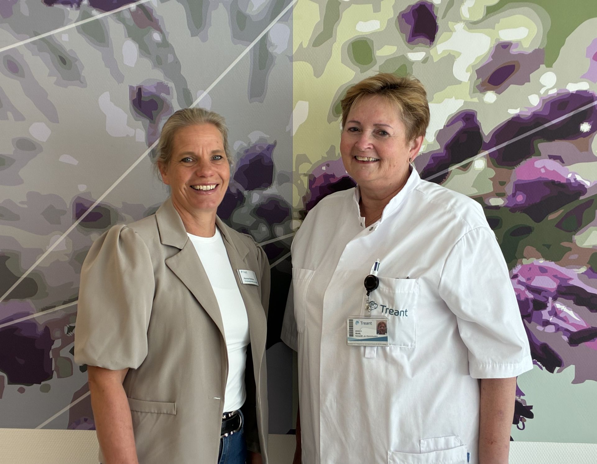 Twee vrouwen poseren samen voor een kleurrijke, abstracte achtergrond.